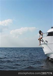 Young woman sitting at edge of yacht with legs dangling overboard side view