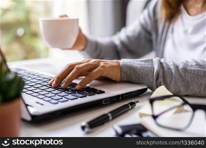 Young woman sitting at living room and working on laptop and smartphone at home