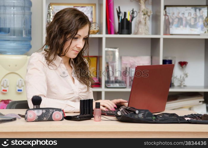 Young woman sitting at office table, laid out on the table cosmetics