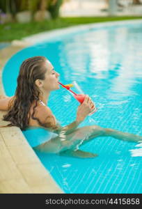 Young woman sitting at pool and drinking cocktail