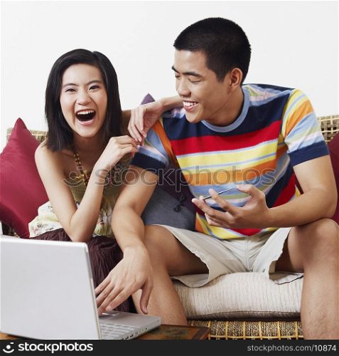 Young woman sitting beside a young man holding a credit card and using a laptop