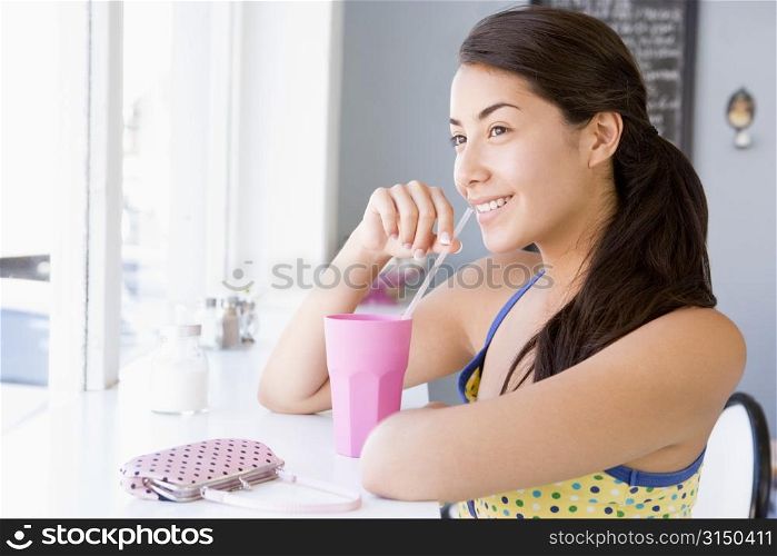 Young woman sitting by a window and having a cold drink