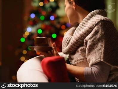 Young woman sitting chair with hot beverage in front of Christmas tree. Rear view