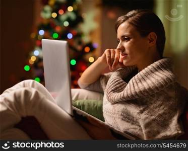 Young woman sitting chair with laptop in front of Christmas tree