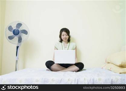 Young woman sitting cross-legged on the bed and using a laptop