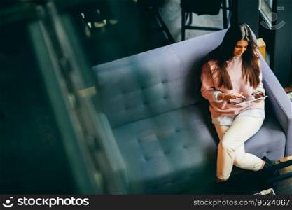 Young woman sitting in a cafe and holding a tablet in the hands. View from above.