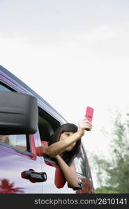 Young woman sitting in a car and taking a picture with a mobile phone