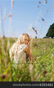Young woman sitting in a field, smiling backwards at the camera