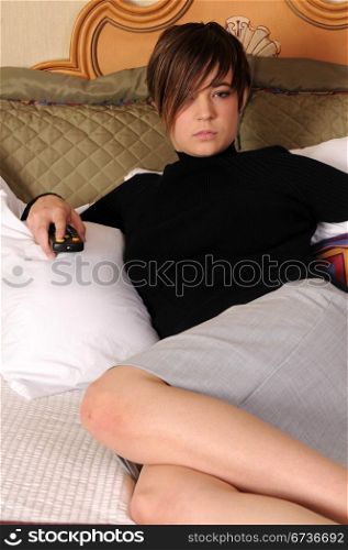 Young woman sitting in a hotel bed with remote in hand