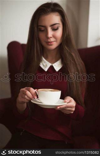 Young woman sitting in a red armchair and drinking fresh coffee. Woman drinking fresh coffee.