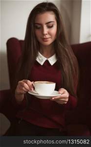 Young woman sitting in a red armchair and drinking fresh coffee. Woman drinking fresh coffee.