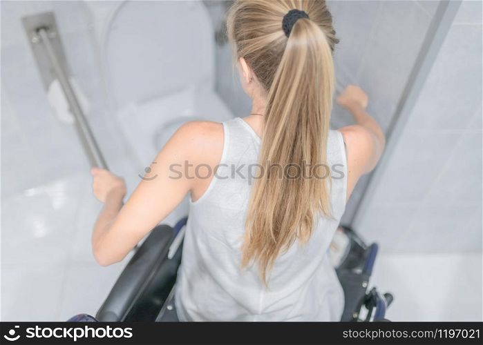 Young woman sitting in a wheelchair grabs the handrails for the disabled. Accessibility concept.. woman moving from wheelchair to bathroom