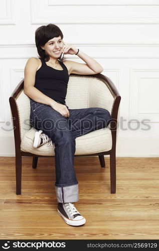 Young woman sitting in an armchair and talking on a mobile phone