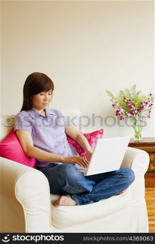 Young woman sitting in an armchair and working on a laptop
