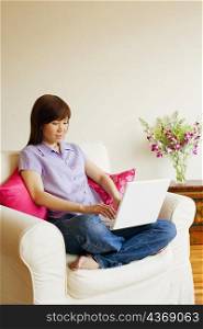 Young woman sitting in an armchair and working on a laptop