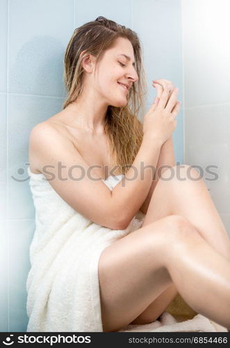 Young woman sitting in bathroom and applying lotion