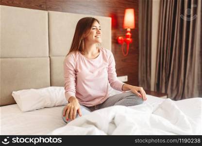 Young woman sitting in bed in yoga pose, morning relaxation, bedroom interoir on background. Woman sitting in bed in yoga pose, morning