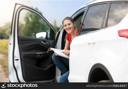 Young woman sitting in car searching for road on map
