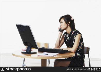 Young woman sitting in front of a computer talking on the telephone