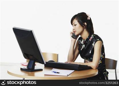 Young woman sitting in front of a computer talking on the telephone