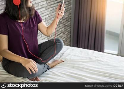 Young woman sitting in her bed and listening music in her bedroom relaxing at home.