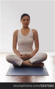 Young woman sitting in lotus position on mat