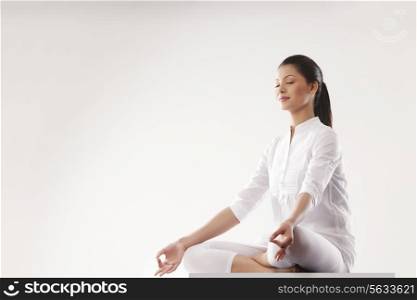 Young woman sitting in lotus position over white background