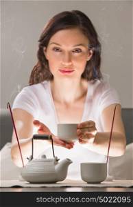 Young woman sitting in meditation pose in front of tea set and aroma sticks. Relaxation concept