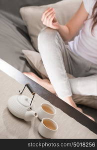 Young woman sitting in meditation pose in front of tea set. Relaxation concept