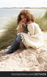 Young Woman Sitting In Sand Dunes Wrapped In Blanket