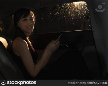 Young woman sitting in the car, on her phone, and looking at the camera on a rainy night in Beijing