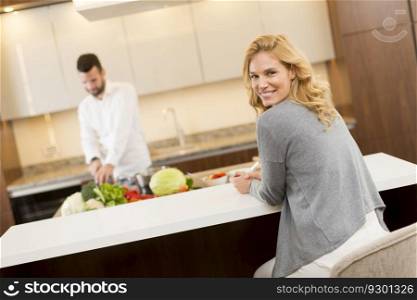 Young woman sitting in the kitchen while the young man prepares food