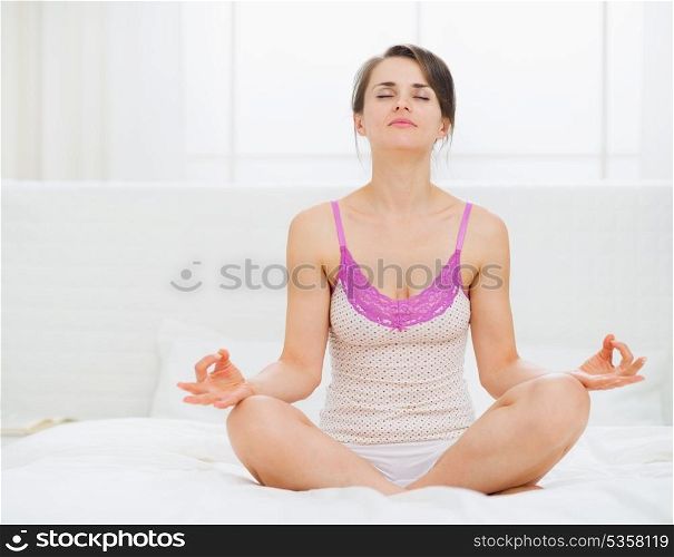 Young woman sitting in yoga pose on bed