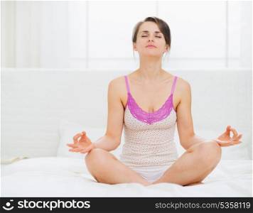 Young woman sitting in yoga pose on bed