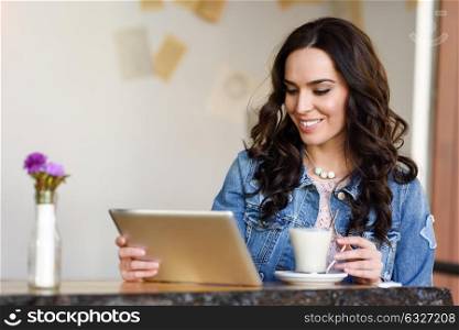 Young woman sitting indoor drinking coffee and looking at her tablet computer. Cool young modern caucasian female in her 20s. Cafe city lifestyle.