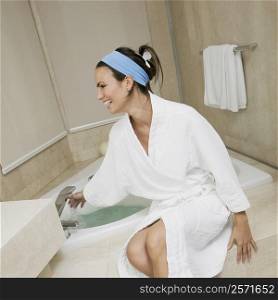 Young woman sitting near a bathtub checking the water temperature