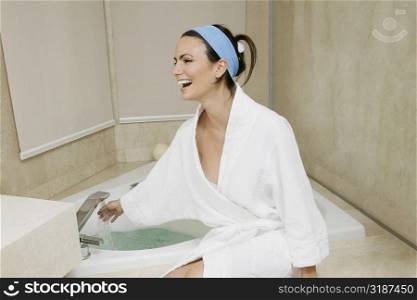 Young woman sitting near a bathtub checking the water temperature