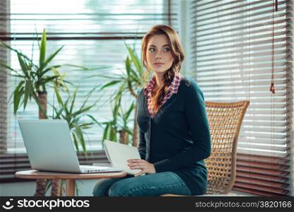 Young woman sitting next to a laptop with a book with a blank cover