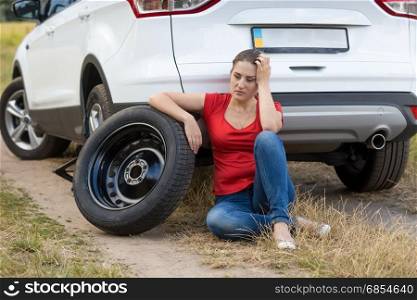 Young woman sitting next to the car with flat tire