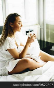 Young woman sitting on a bed and drinking coffee after waking up