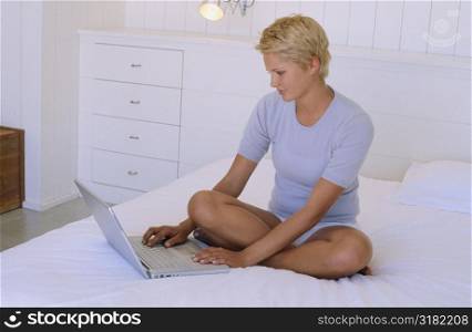 Young woman sitting on a bed with a laptop