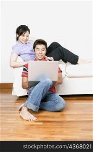 Young woman sitting on a couch with a mid adult man using a laptop