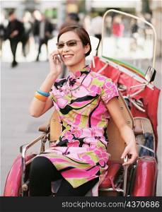 Young woman sitting on a pedicab and talking on a mobile phone