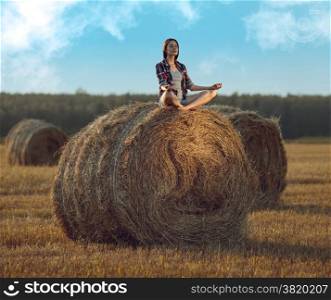 Young woman sitting on a stack of hay and meditating in sunlight