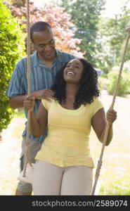 Young woman sitting on a swing and a mid adult man standing behind her