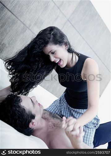 Young woman sitting on a young man and holding his hands in bed