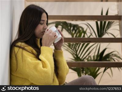 young woman sitting on an indoor staircase having a cup of coffee
