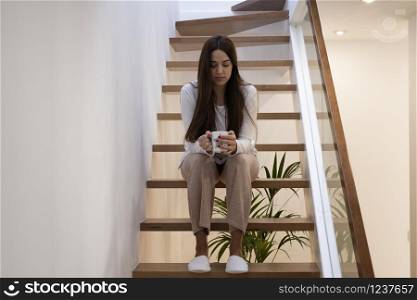 young woman sitting on an indoor staircase having a cup of coffee