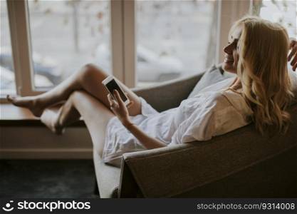 Young woman sitting on armchair and using mobile phone in the room