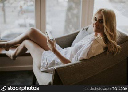 Young woman sitting on armchair and using mobile phone in the room
